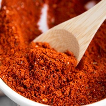 close up of homemade taco seasoning on small wooden spoon in white bowl