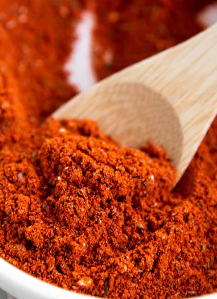 close up of homemade taco seasoning on small wooden spoon in white bowl