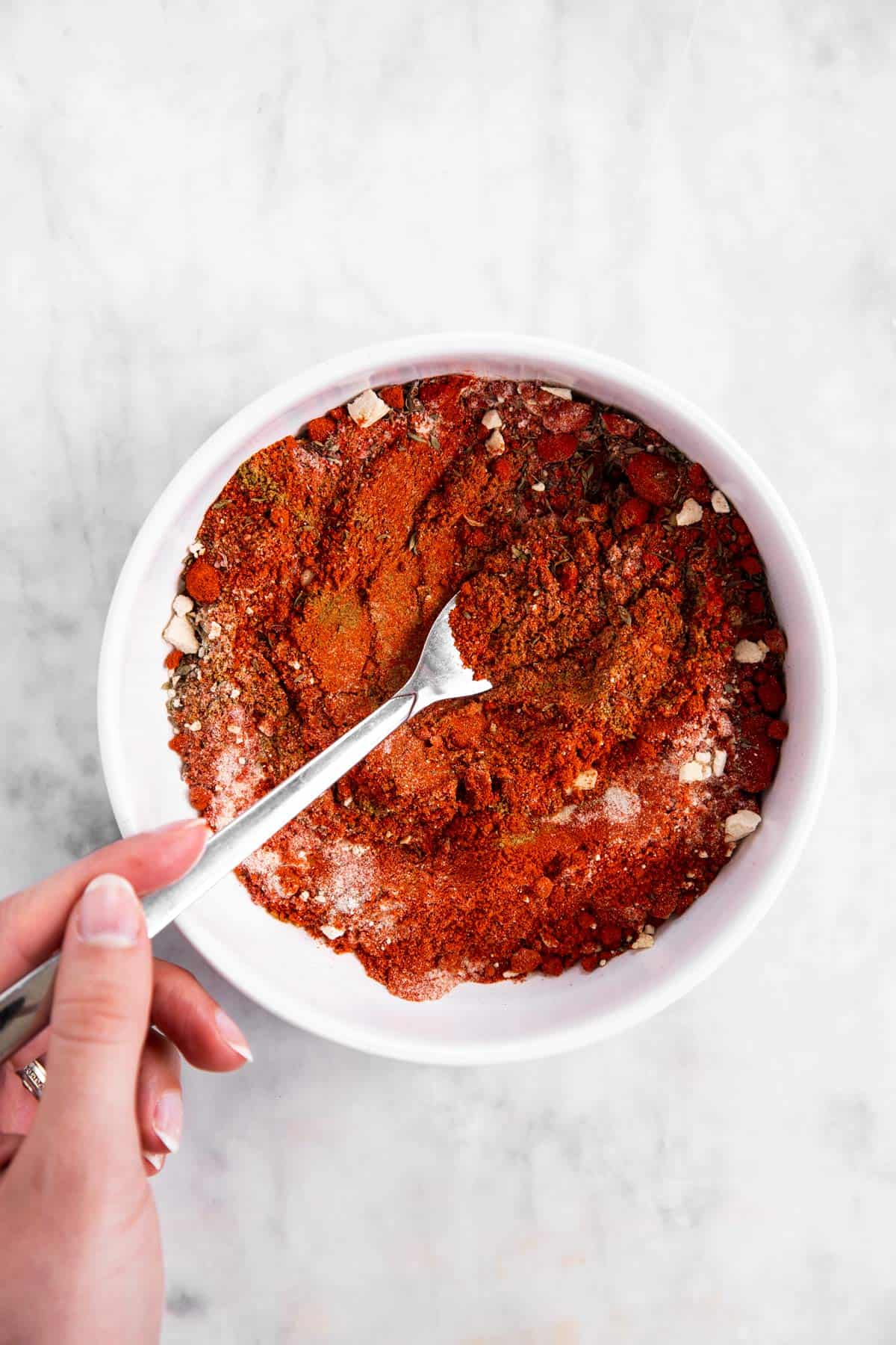 female hand combining spices for taco seasoning in white bowl with a fork