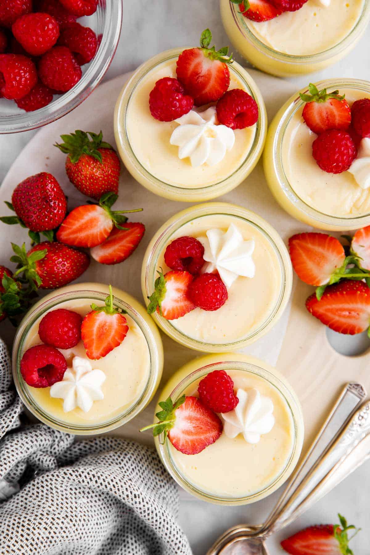 six individual vanilla pudding cups on serving platter with fresh berries