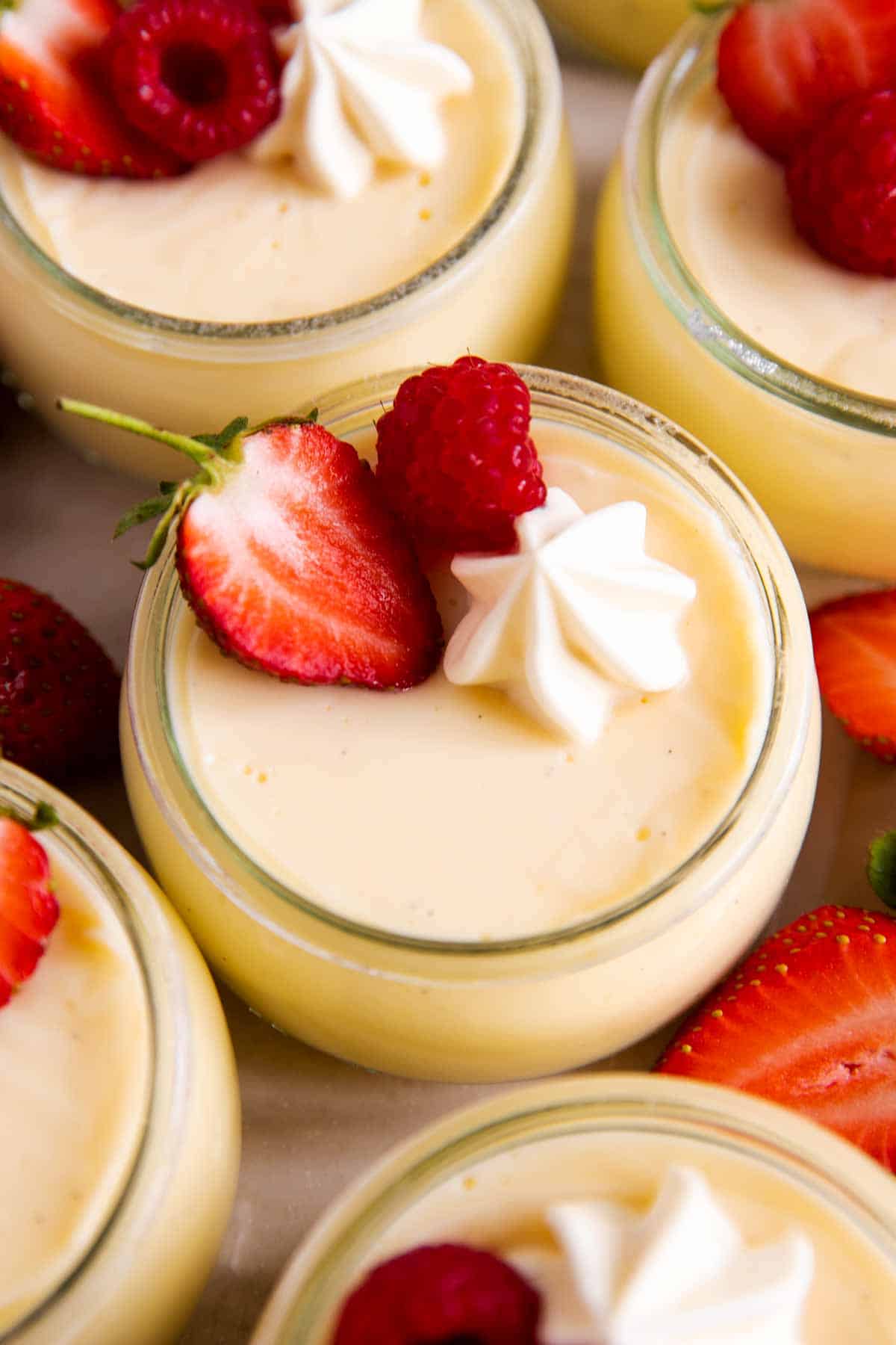 several glass jars with homemade vanilla pudding and fresh berries on white surface