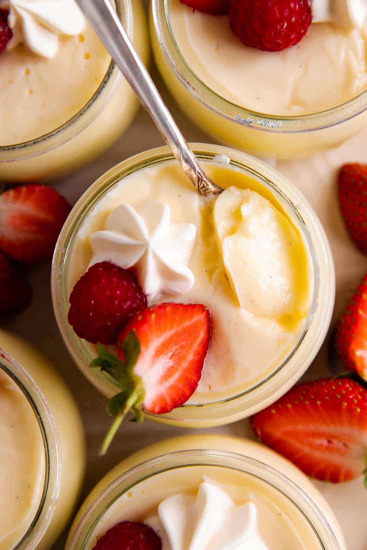 overhead view of spoon in vanilla pudding in glass jar with fresh berries