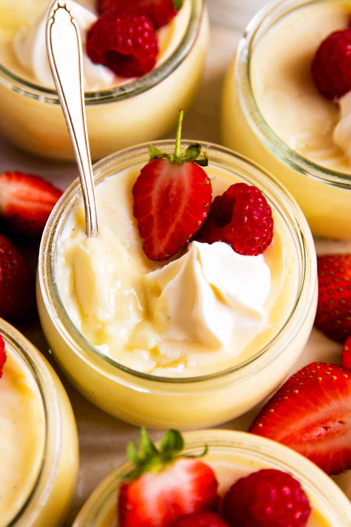 jar of homemade vanilla pudding topped with cream and berries with spoon stuck inside