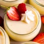 several glass jars with homemade vanilla pudding and fresh berries on white surface