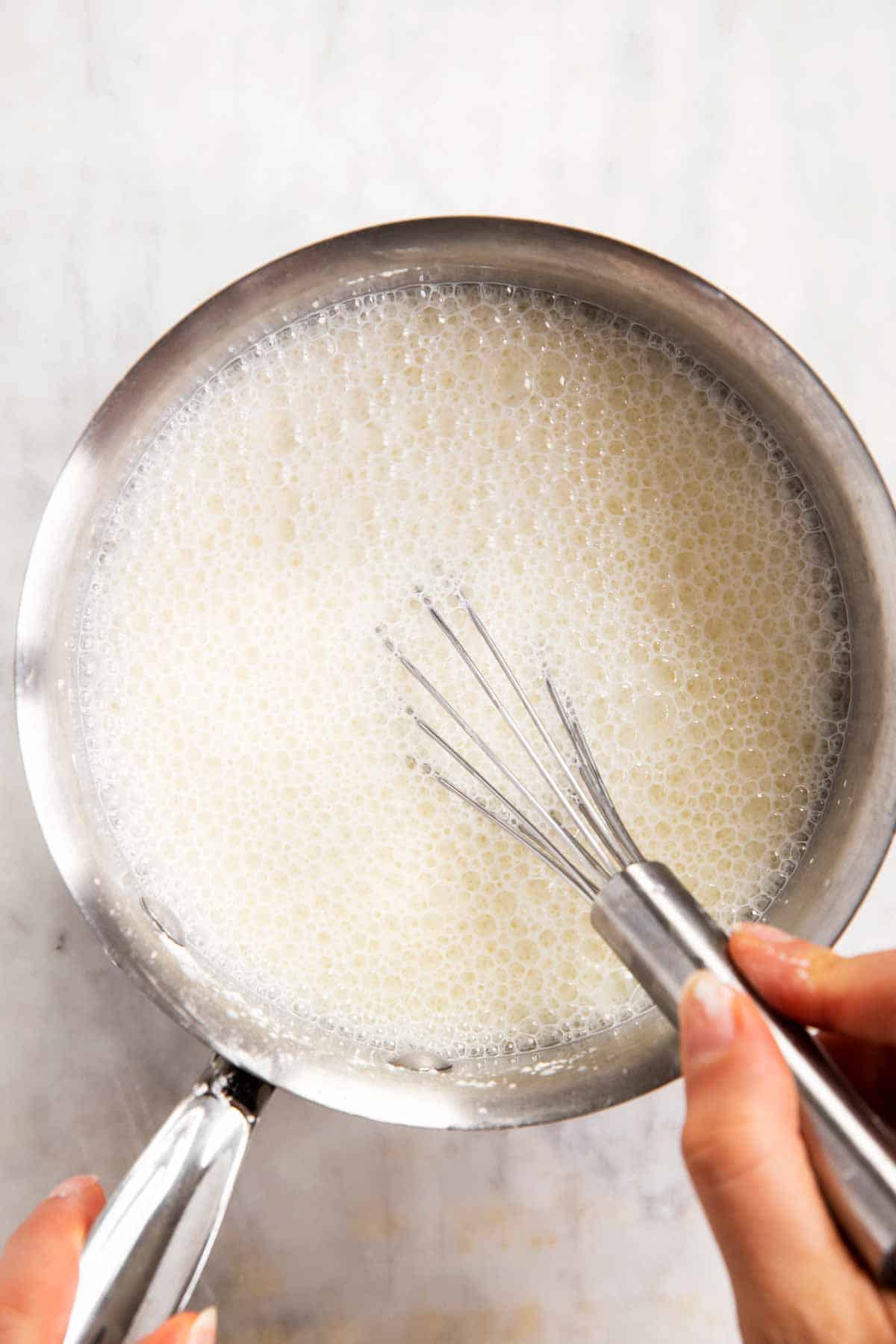 female hands whisking milk in saucepan