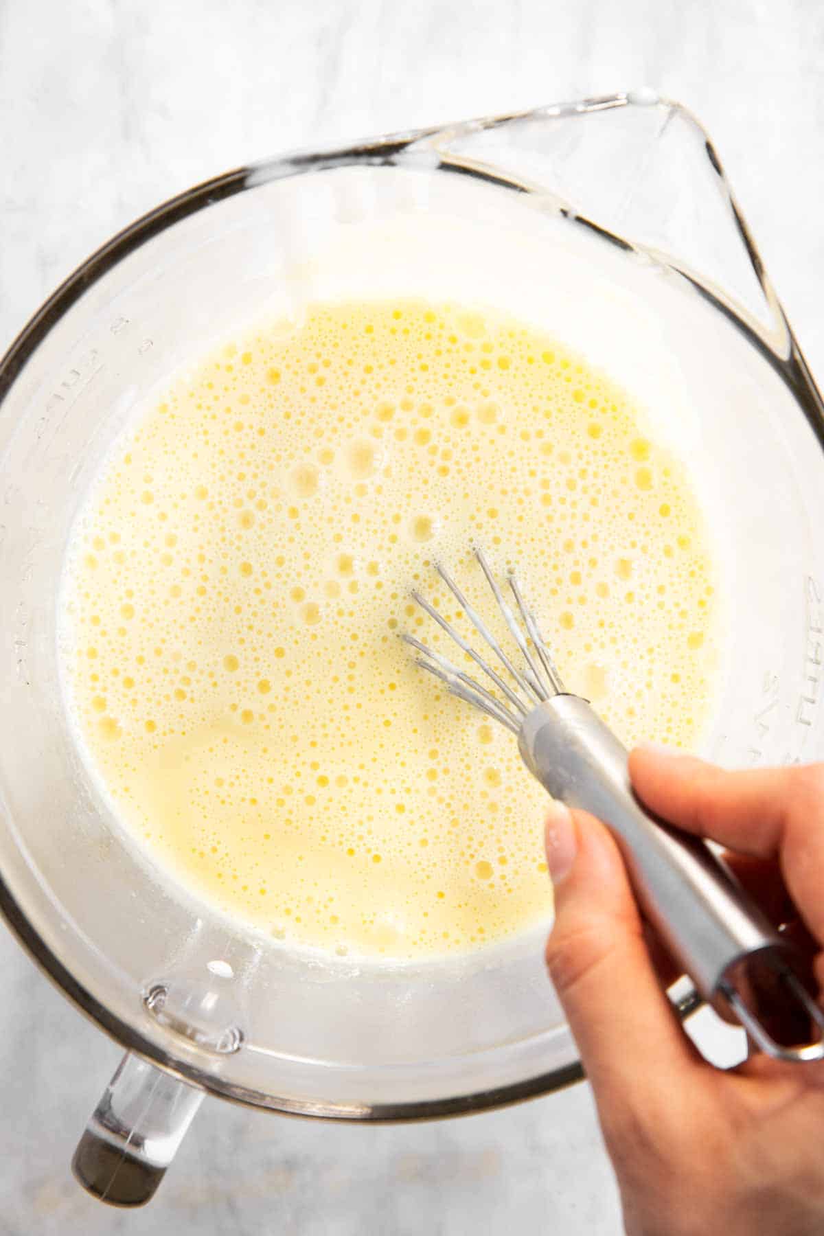 female hand whisking vanilla pudding mixture in glass bowl