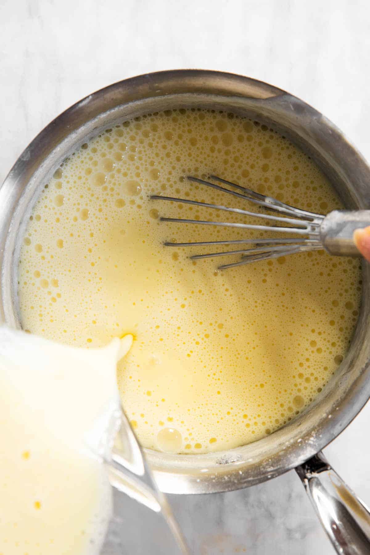 vanilla pudding mixture pouring from glass bowl into saucepan