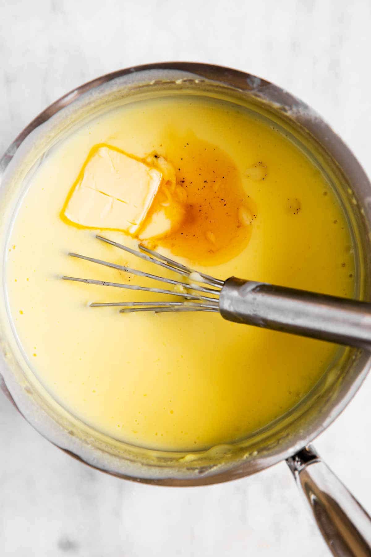 overhead view of vanilla pudding in saucepan with vanilla extract and butter on top