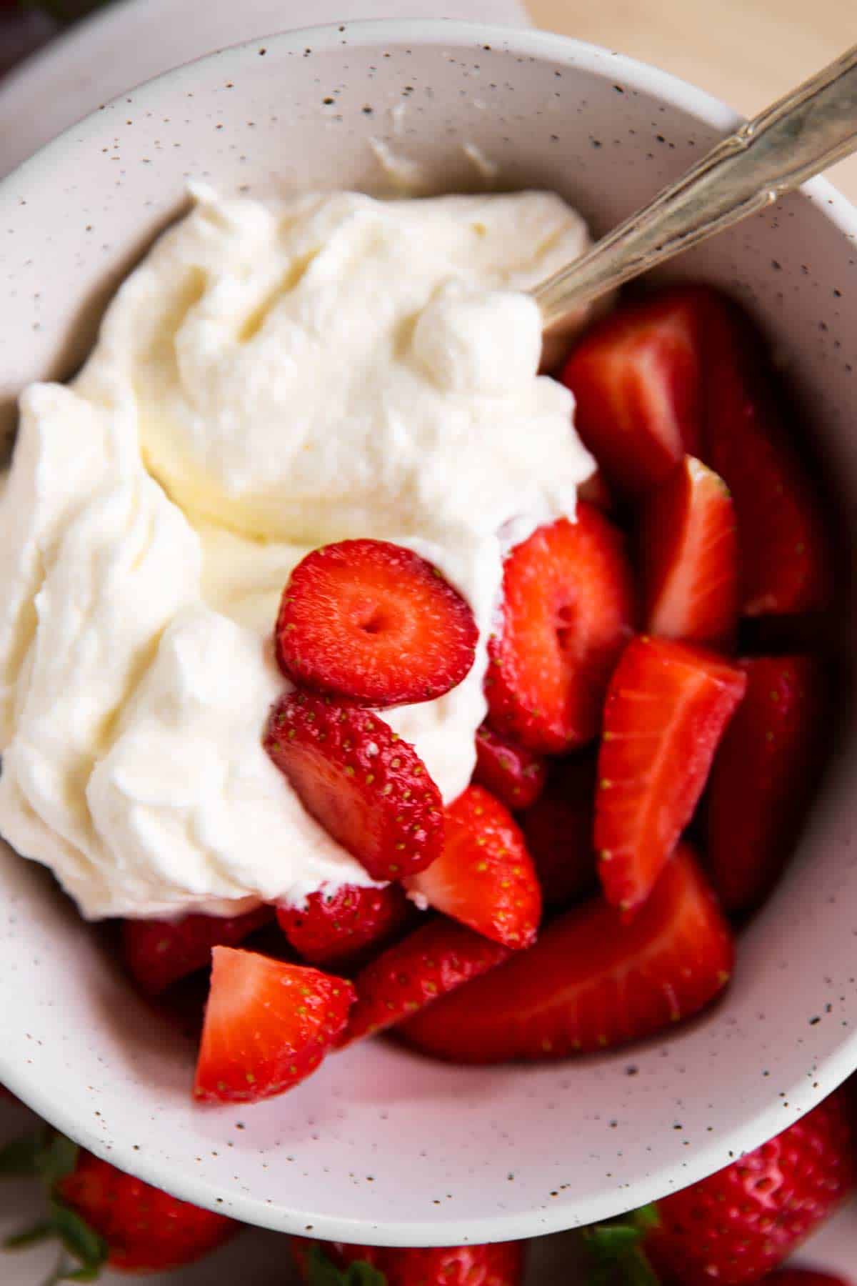 overhead view of fresh sliced strawberries and whipped cream in a white bowl with a spoon