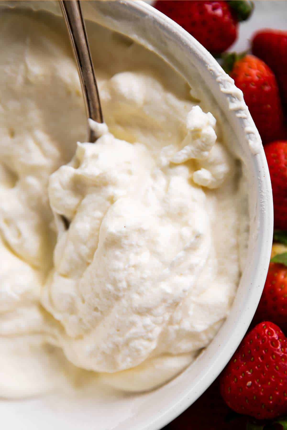 overhead view of whipped cream in white bowl with spoon next to fresh strawberries