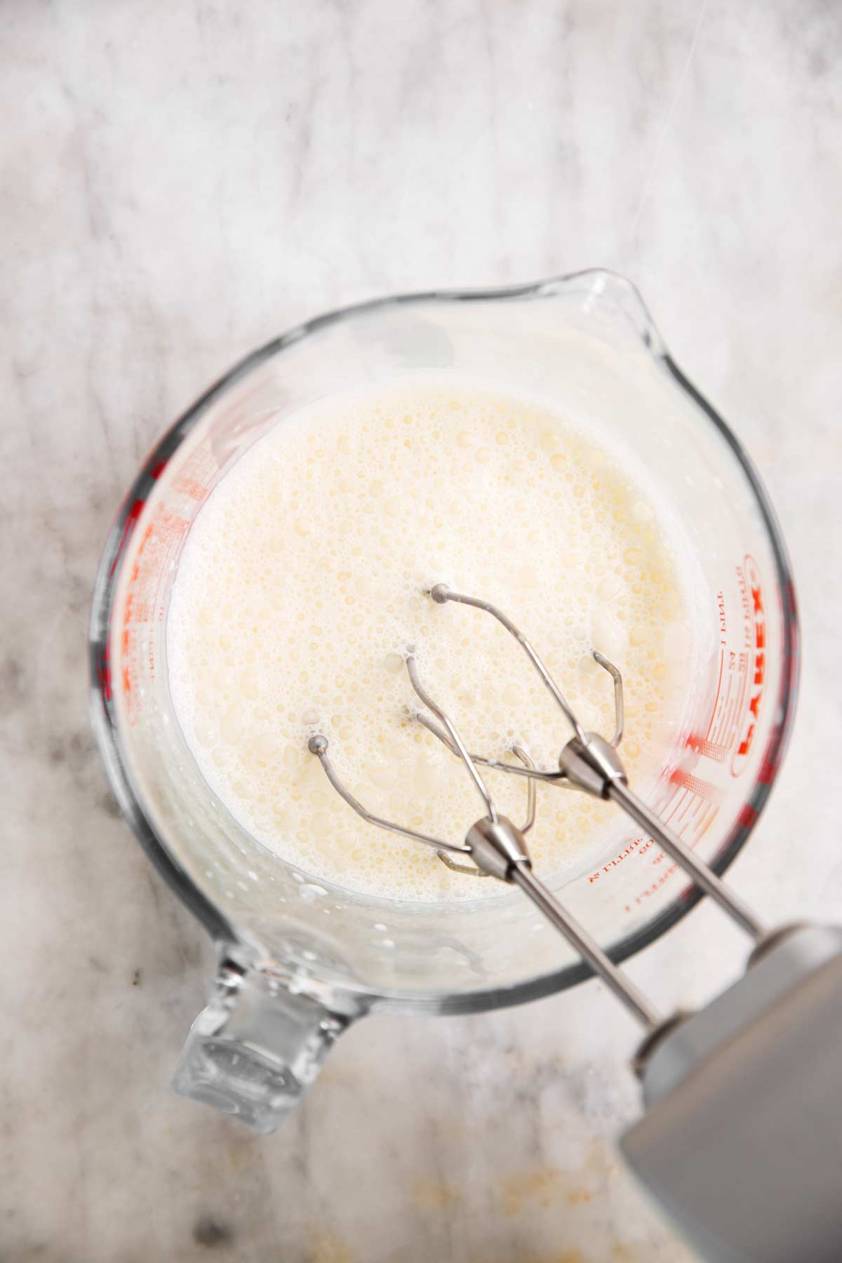 frothy whipped cream in glass measuring jug with hand mixer beaters inside