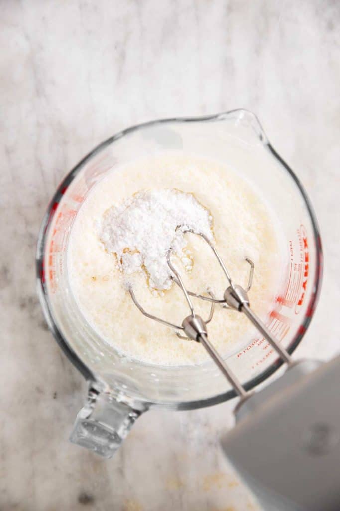 frothy cream with icing sugar and vanilla in glass measuring jug