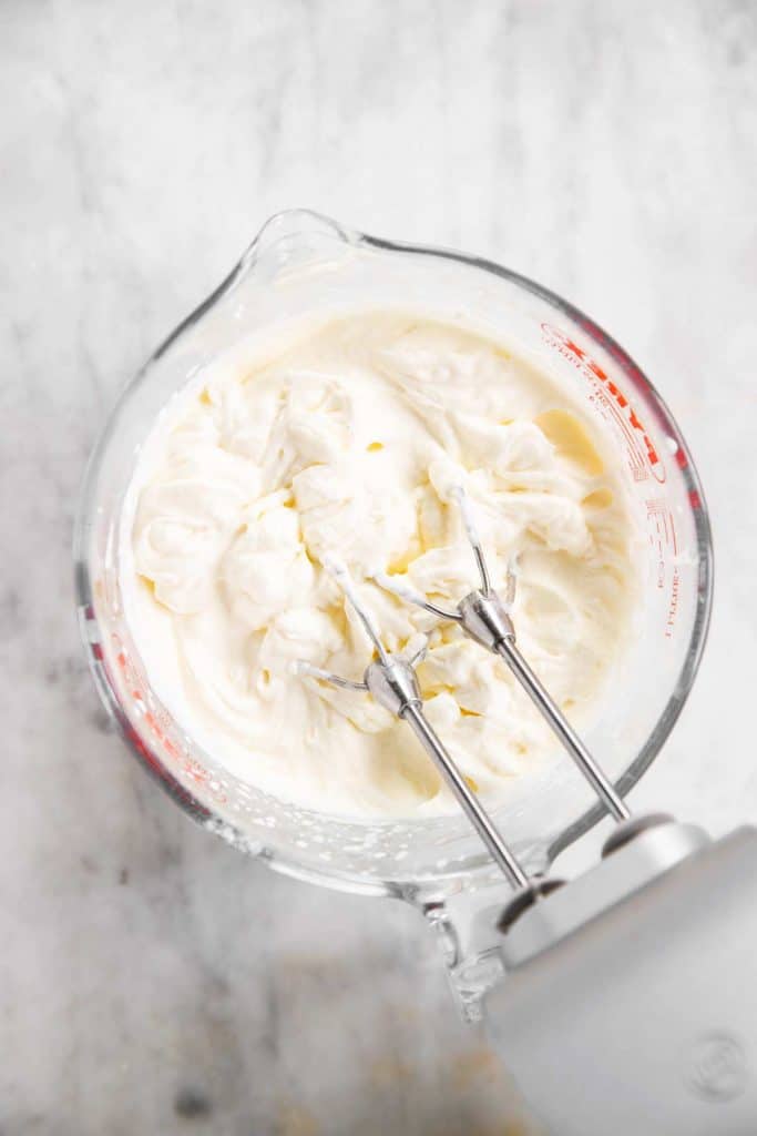 homemade whipped cream in glass measuring jug after three minutes of whipping