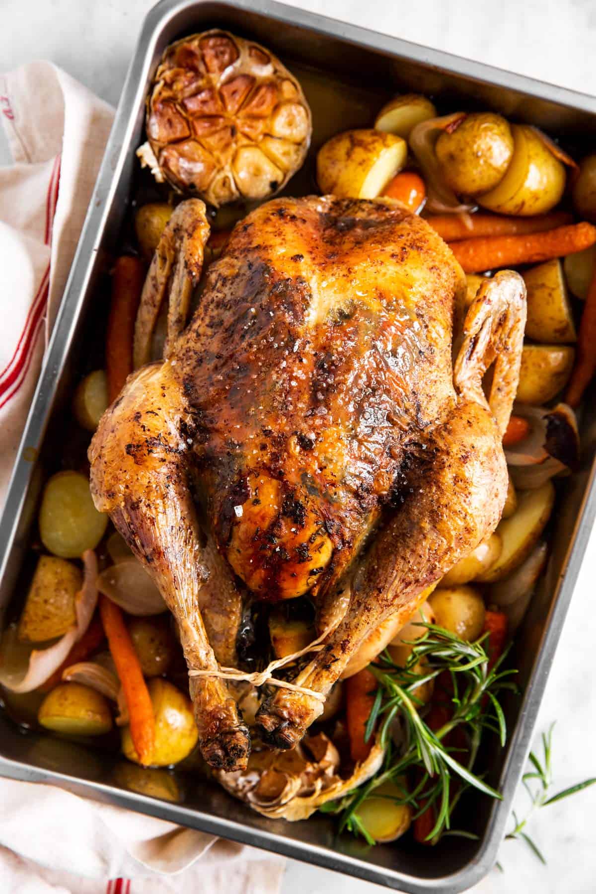 overhead view of whole roasted chicken in roasting pan with carrots and potatoes