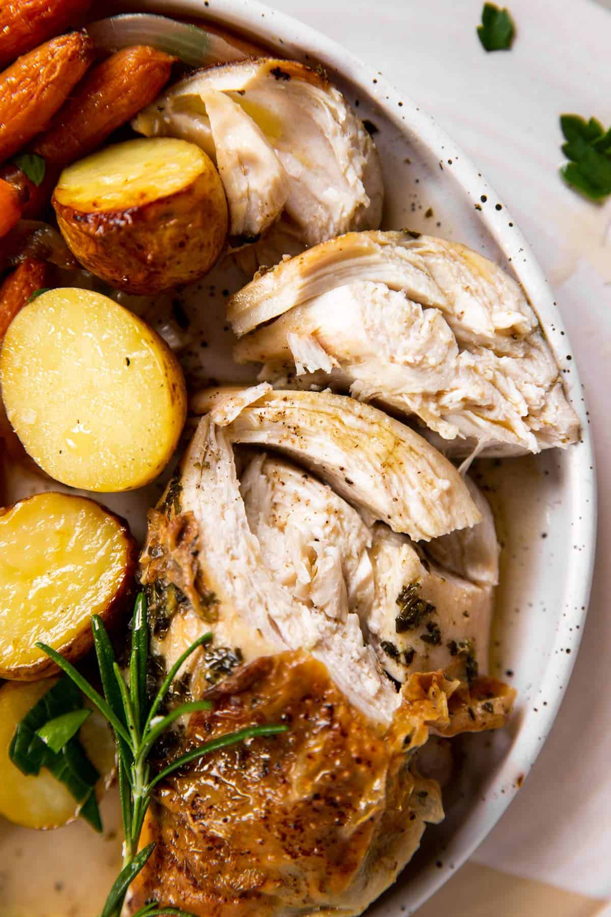 overhead closeup view of carved chicken breast on white plate next to potatoes and carrots