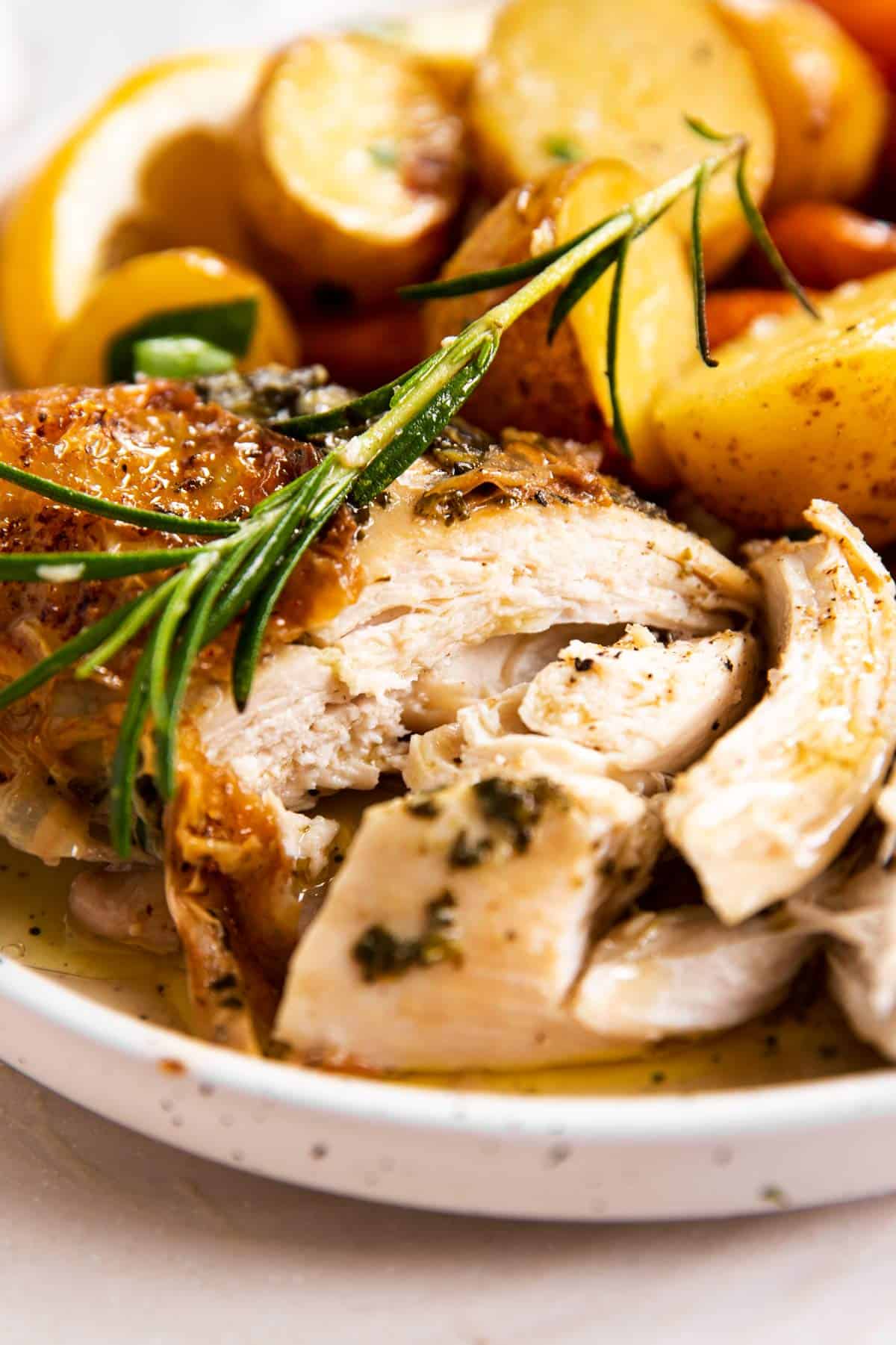 close up view of sliced roasted chicken breast on plate with fresh rosemary, carrots and potatoes