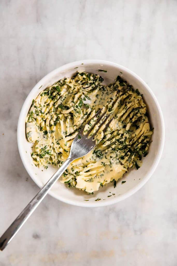 overhead view of white bowl with garlic butter herb butter and a fork