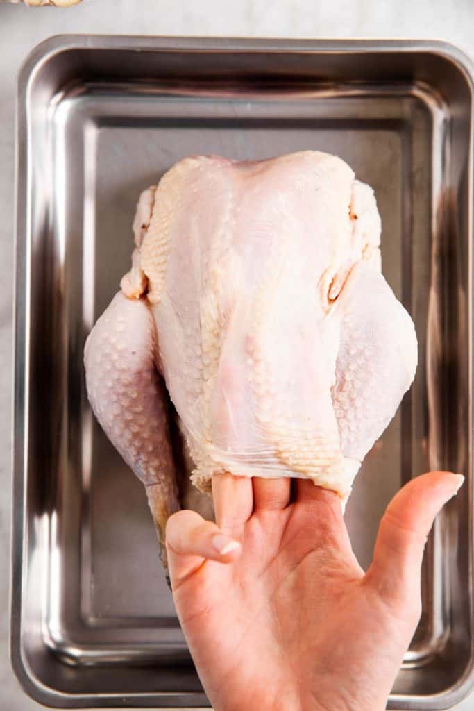 female hand loosening chicken skin on a whole raw chicken