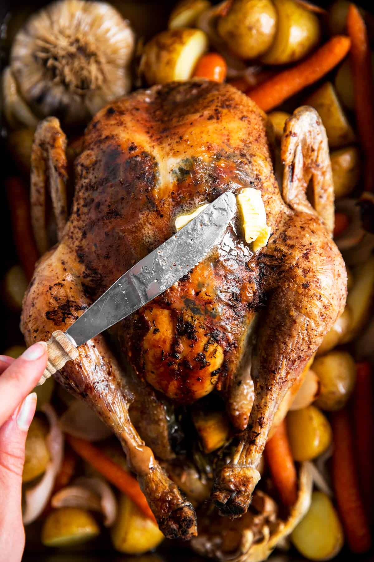 female hand using butter knife to brush butter over roasted chicken