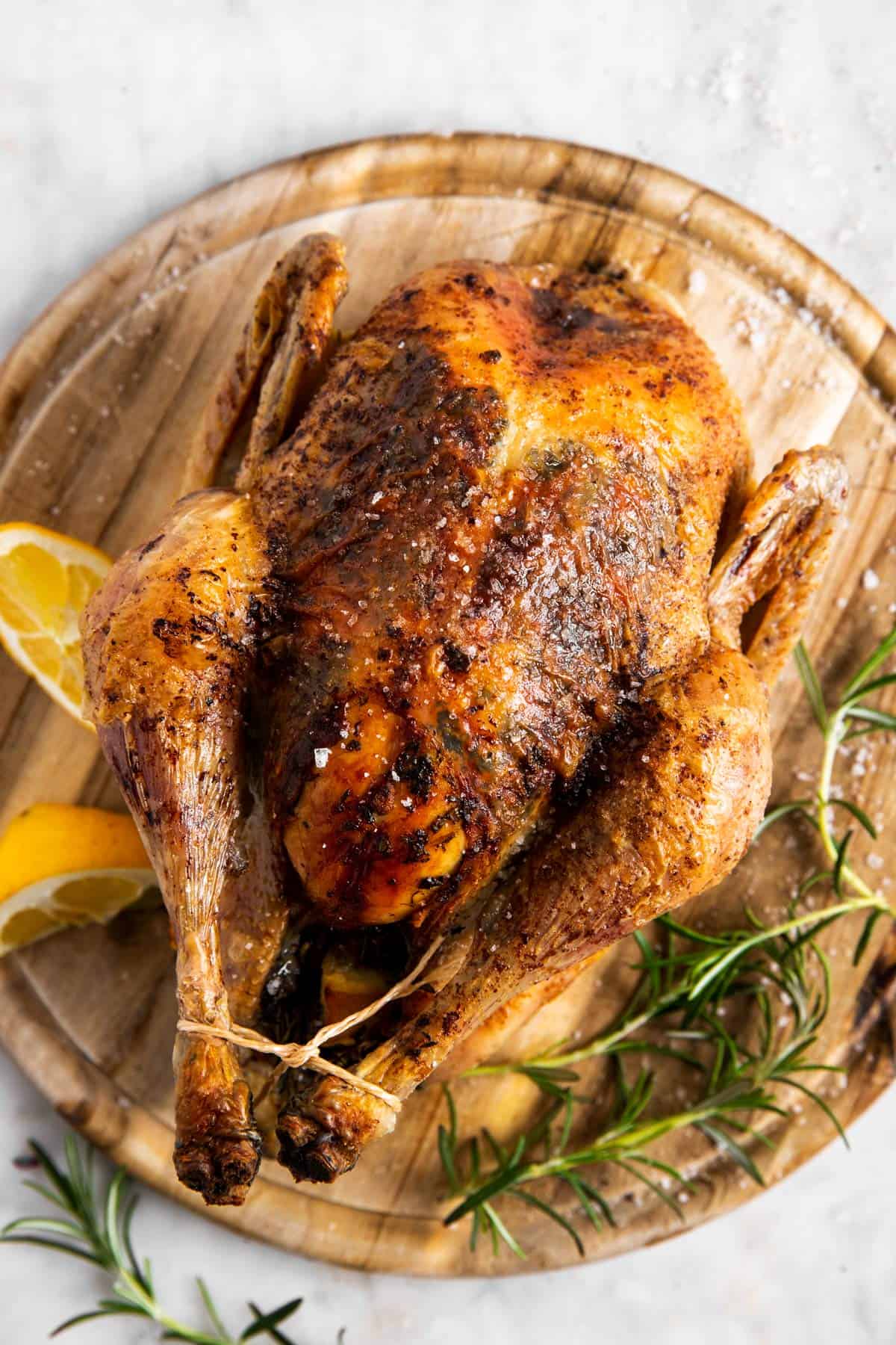 whole roasted chicken resting on round wooden chopping board 