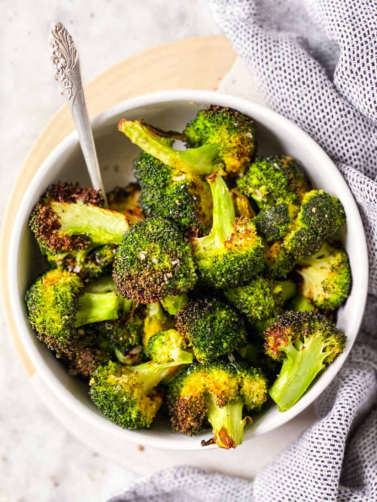 air fried broccoli in white bowl next to cloth napkin