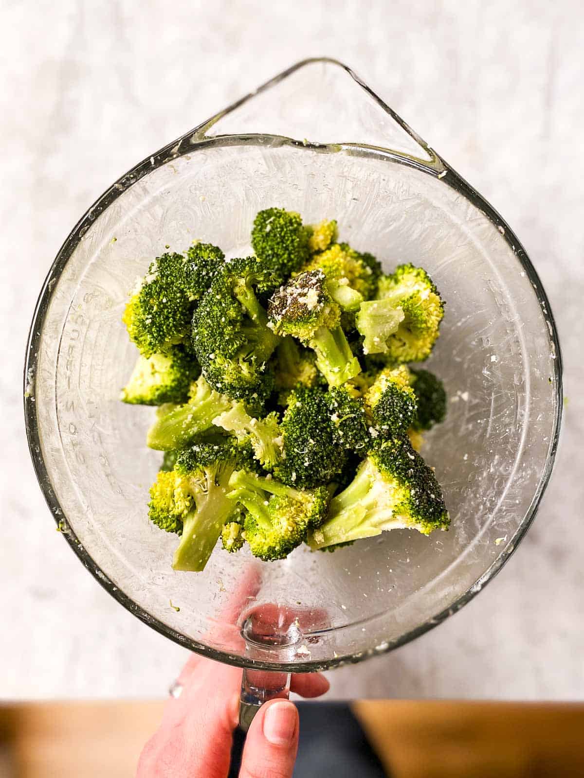 female hand holding glass bowl with seasoned broccoli