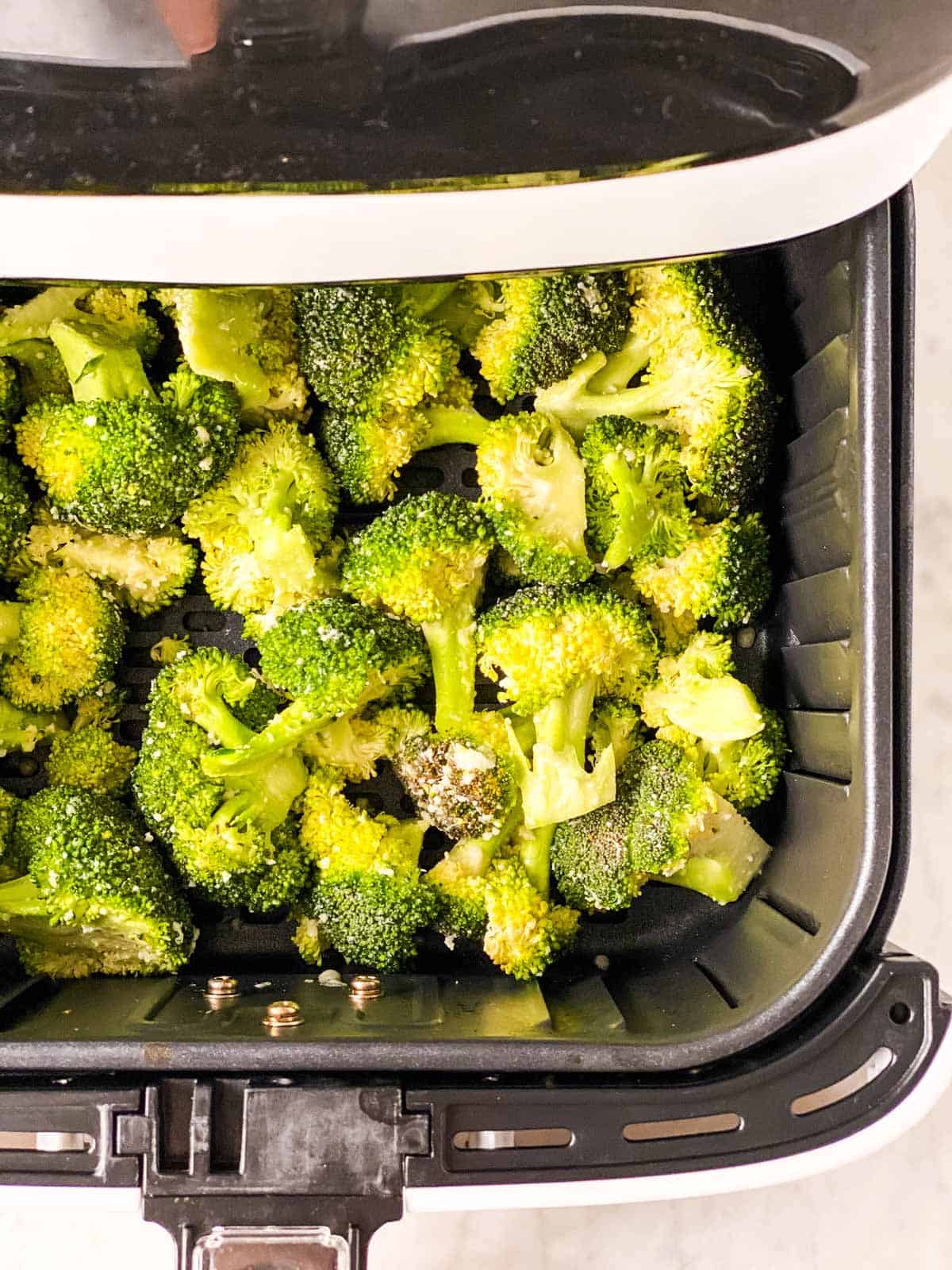 air fryer basket with raw broccoli florets inside