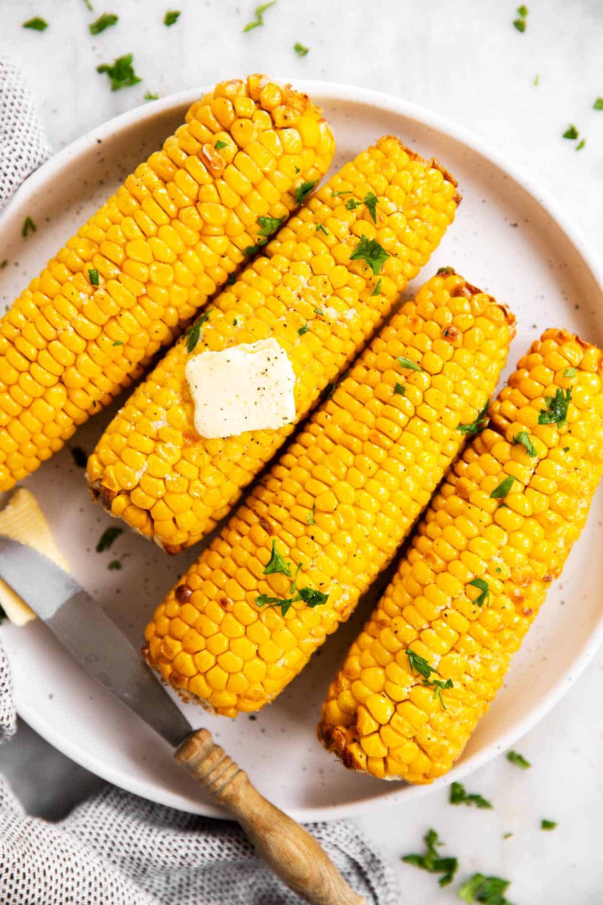 four air fried ears of corn on white plate with butter and parsley