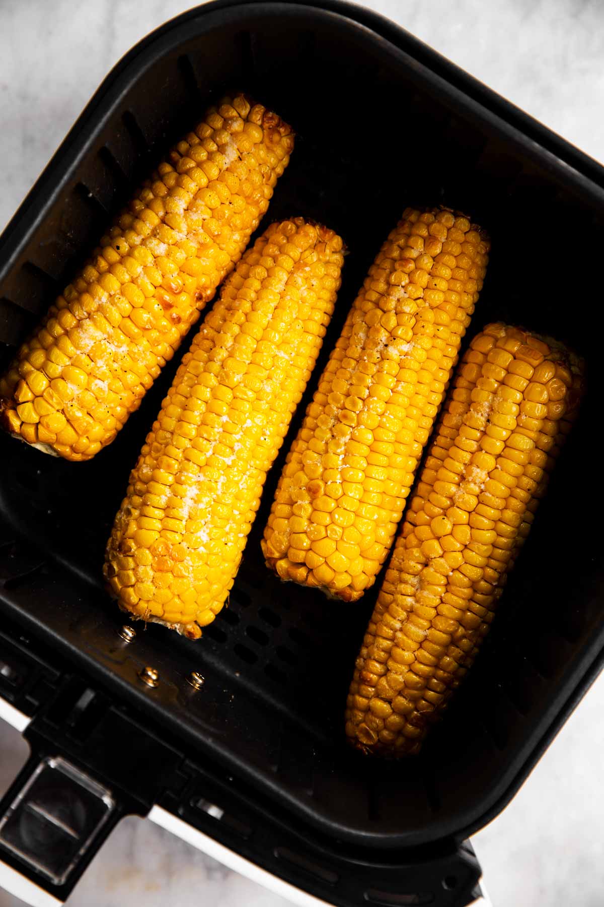 four cooked ears of corn in air fryer basket