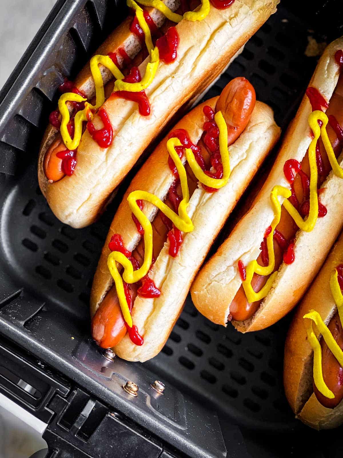 close up photo of hot dogs in air fryer basket with mustard and ketchup