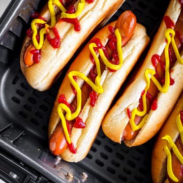 close up photo of hot dogs in air fryer basket with mustard and ketchup