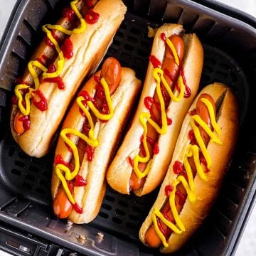 overhead view of four hot dogs garnished with ketchup and mustard in square air fryer basket