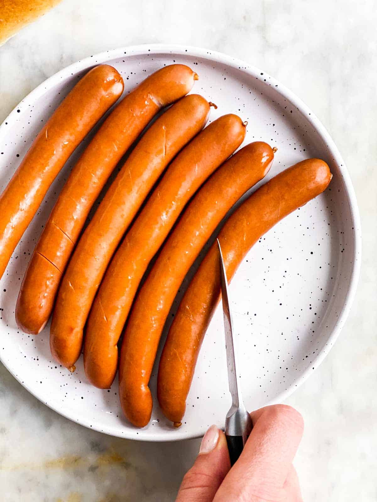 female hand cutting slit into a hot dog