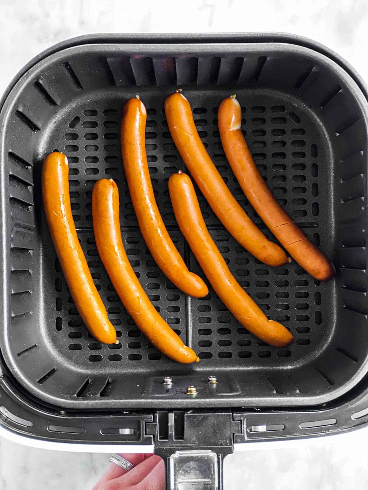 six uncooked hot dogs in air fryer basket