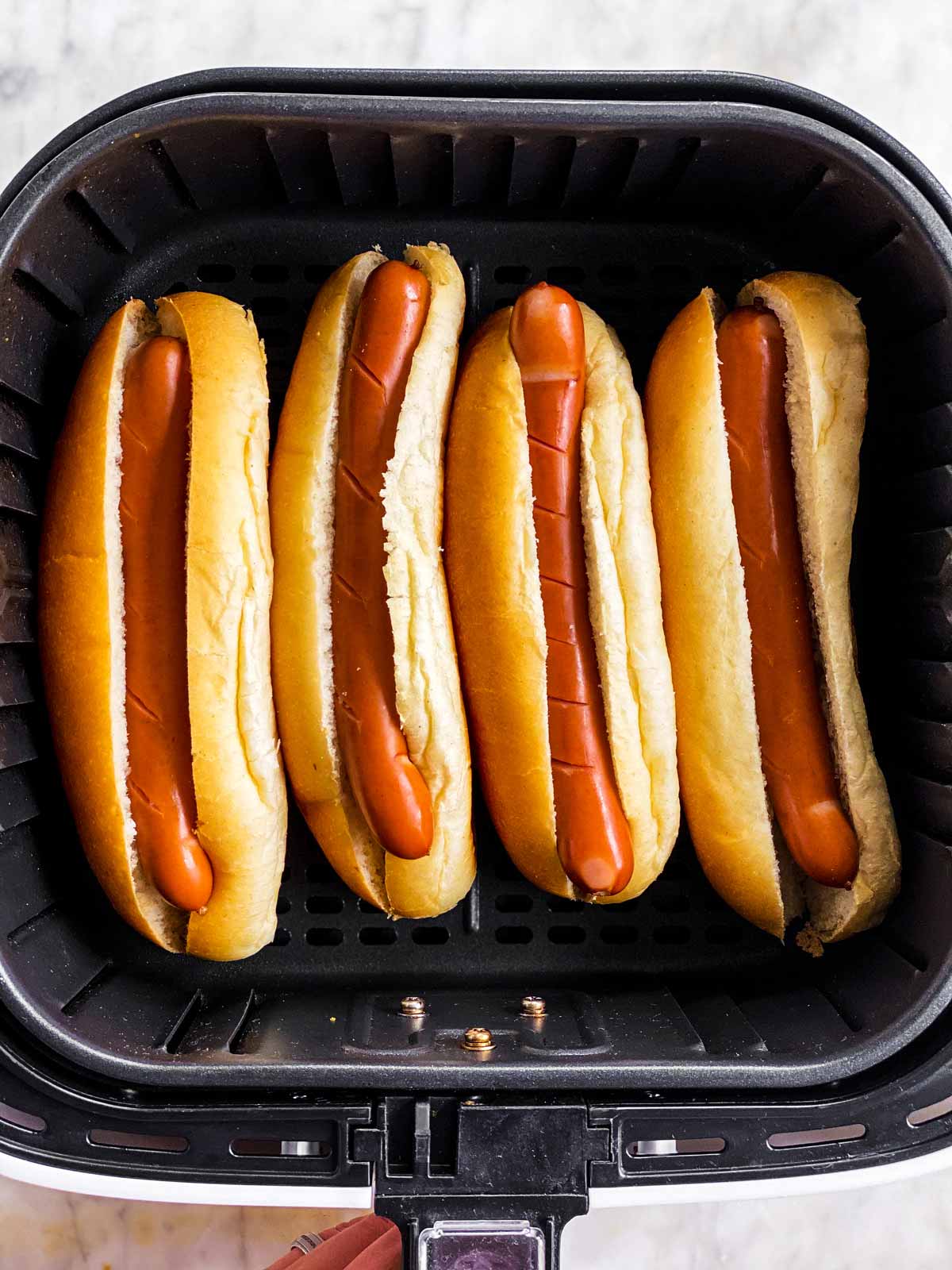 four hot dogs in buns in air fryer basket