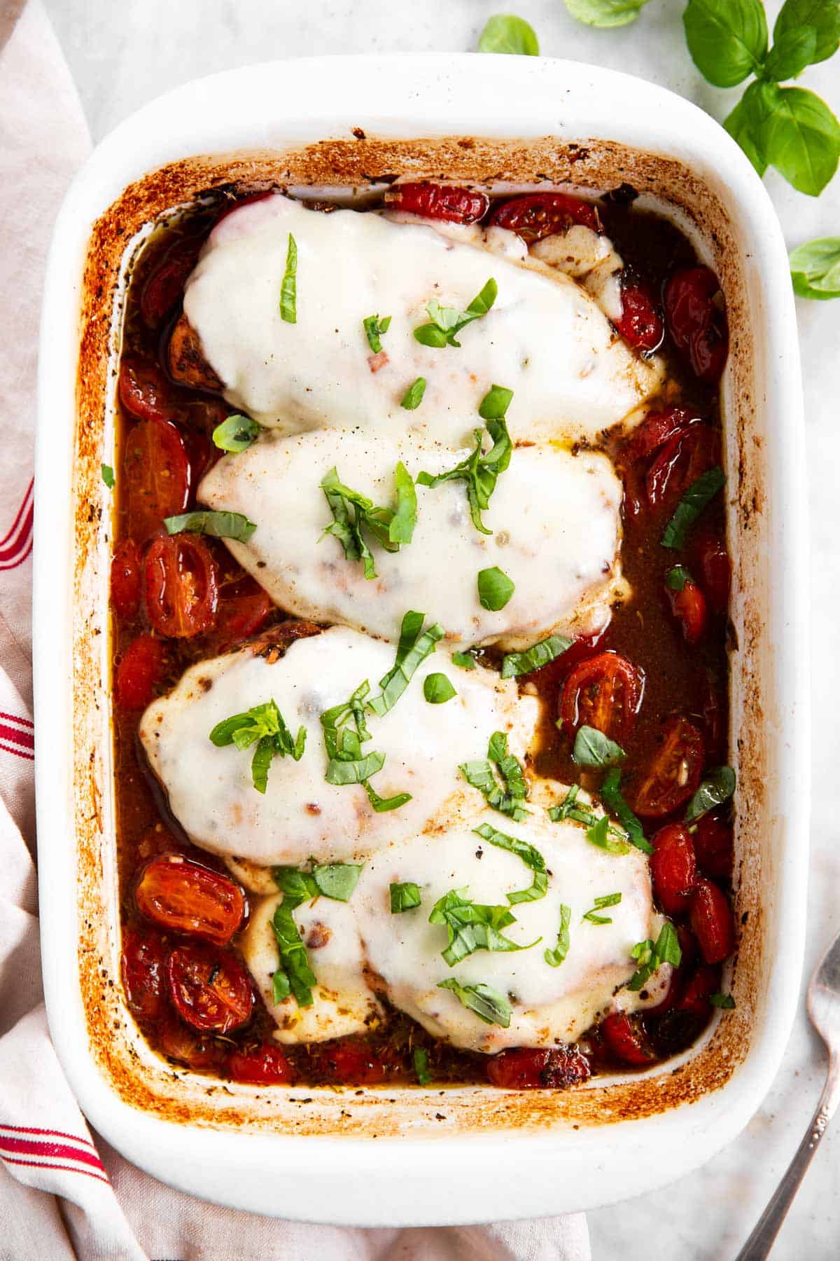 baked caprese chicken in white casserole dish with fresh basil