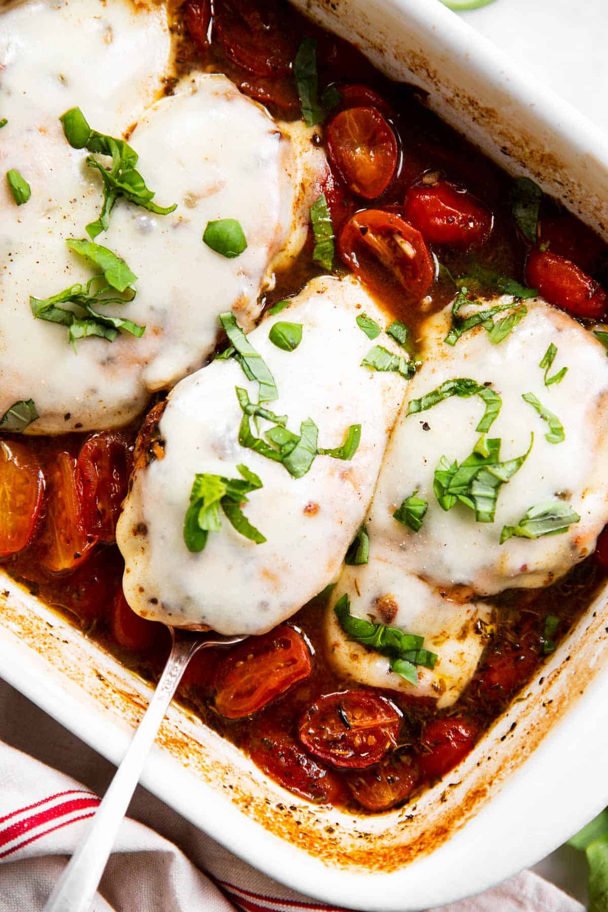 overhead view of baked caprese chicken in white ceramic casserole dish, garnished with fresh basil