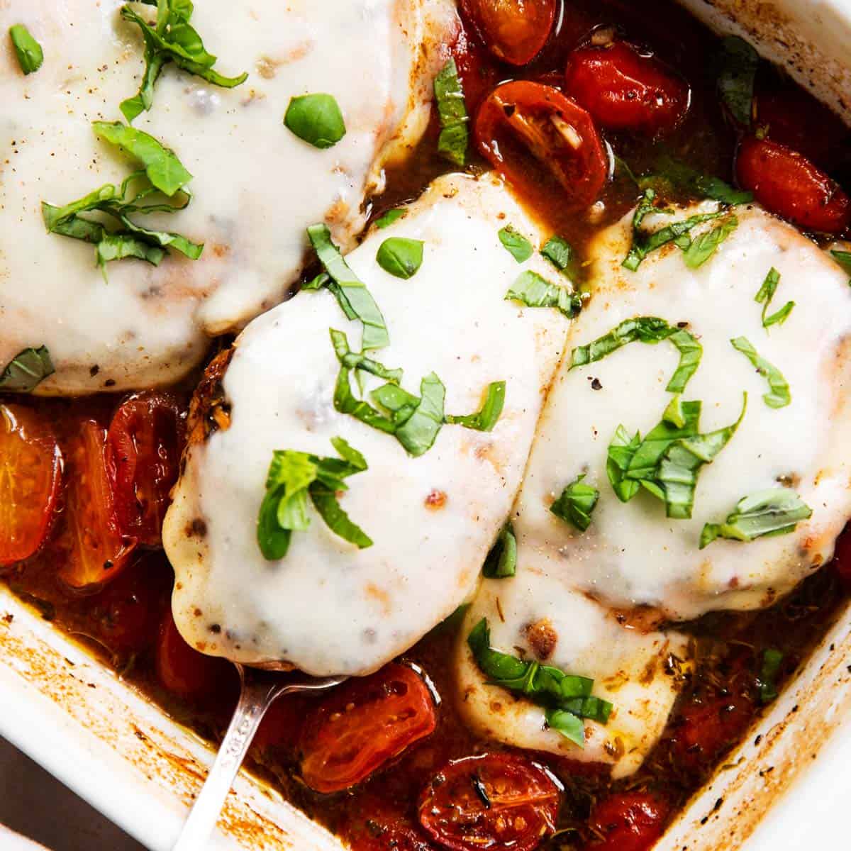 overhead view of baked caprese chicken in white ceramic casserole dish, garnished with fresh basil