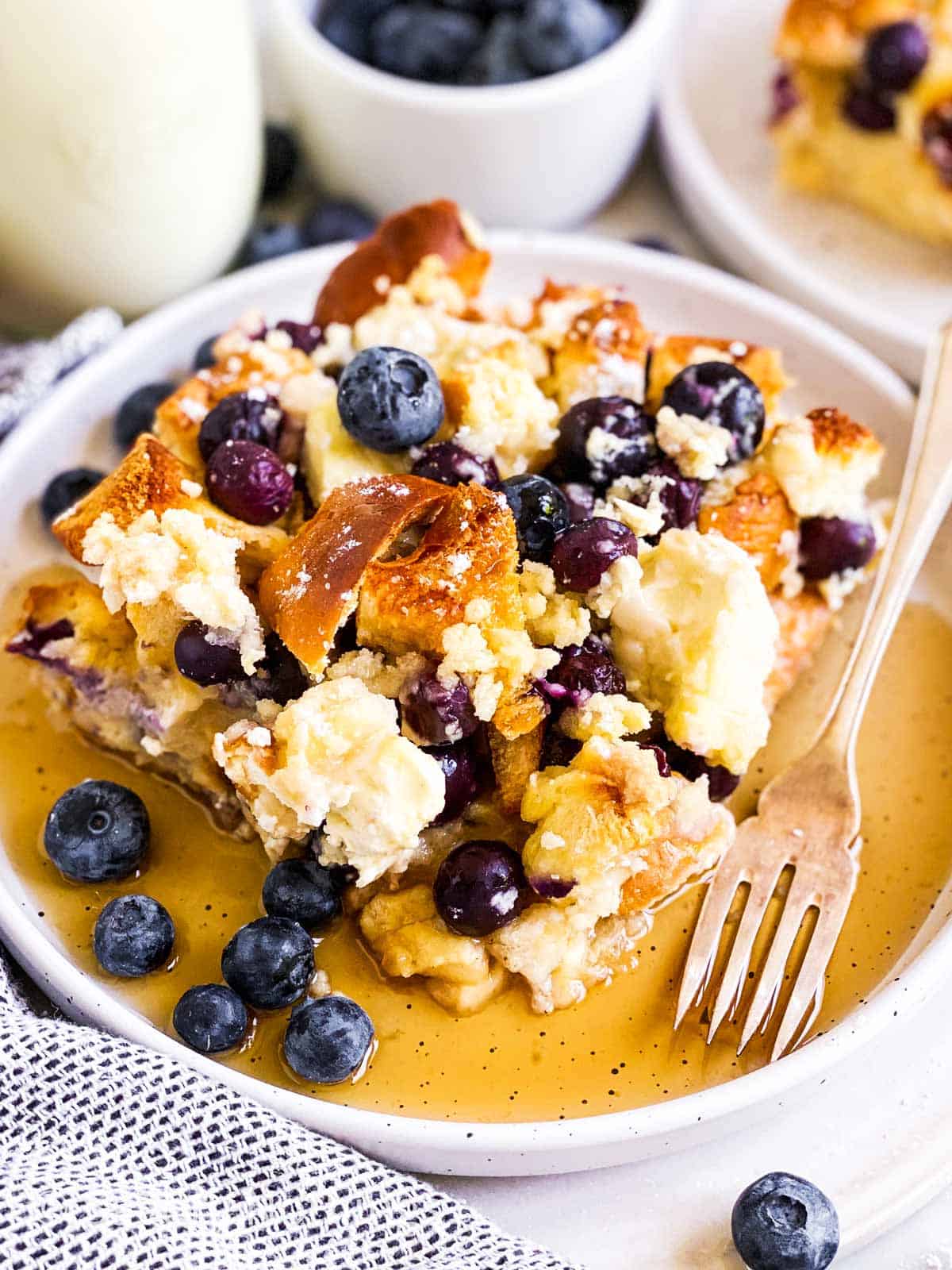 slice of blueberry French toast casserole with maple syrup on white plate