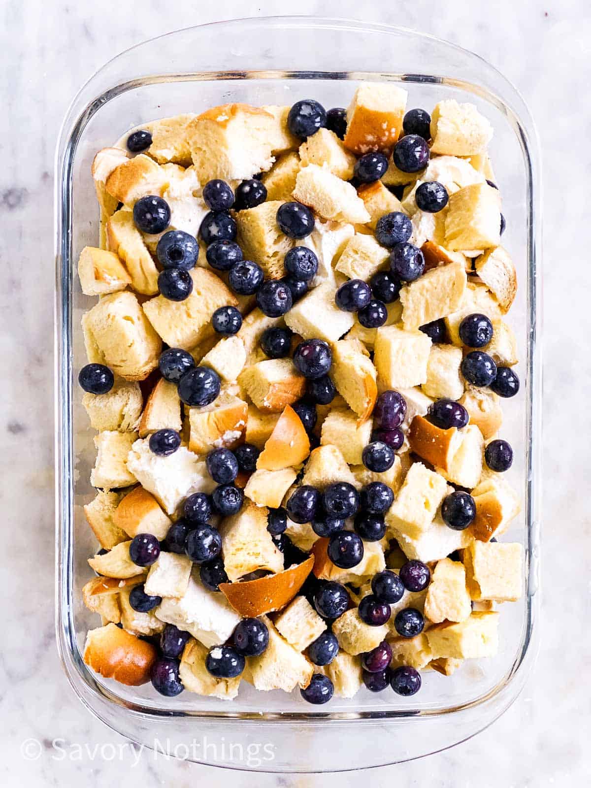 assembled but unbaked blueberry French toast casserole in glass dish sitting on white marble surface