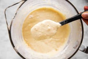 female hand holding spatula with pancake batter over glass bowl