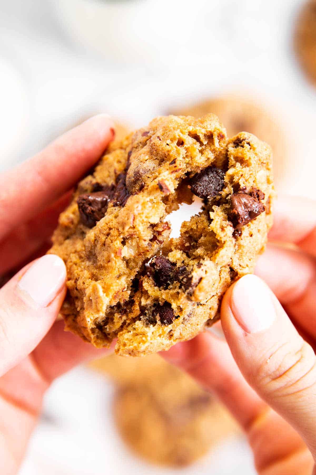 female hands breaking oatmeal chocolate chip cookie in half