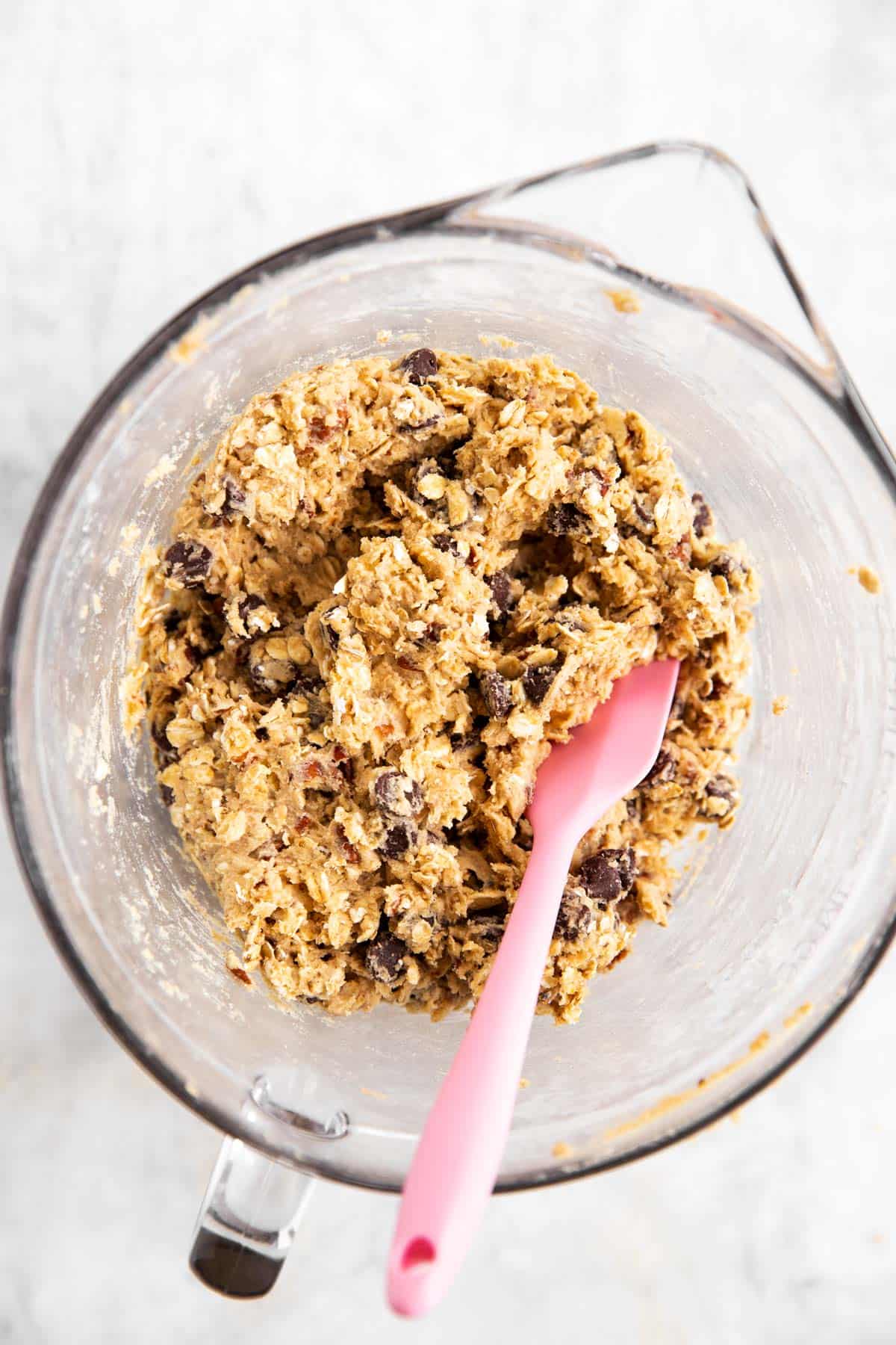 oatmeal chocolate chip cookie dough in glass bowl with pink spatula stuck in