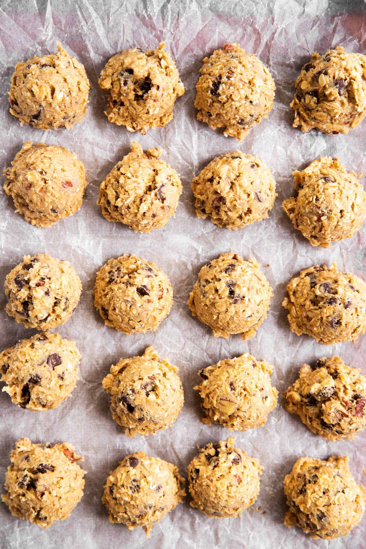 twenty oatmeal chocolate chip cookie dough balls on lined baking sheet