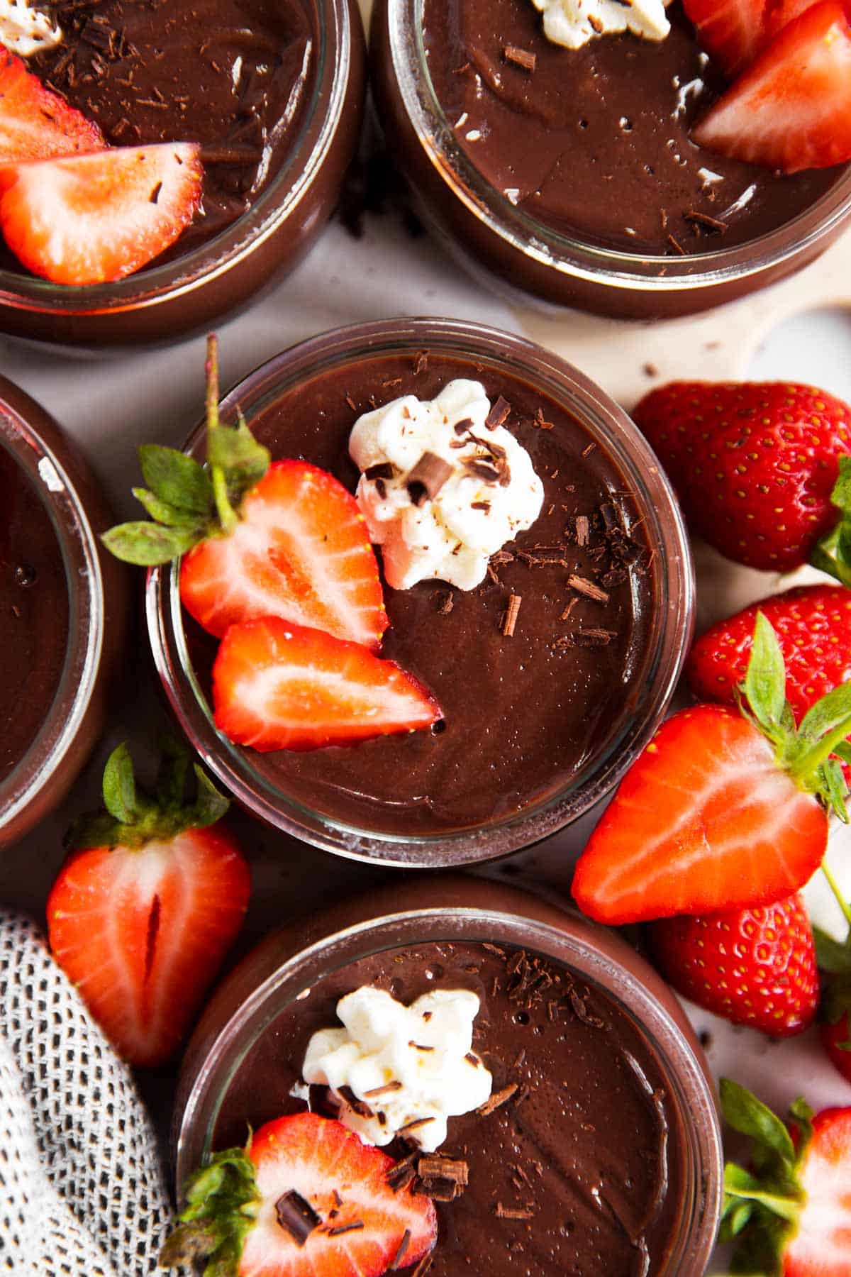 overhead view of several jars with chocolate pudding, garnished with whipped cream and strawberries