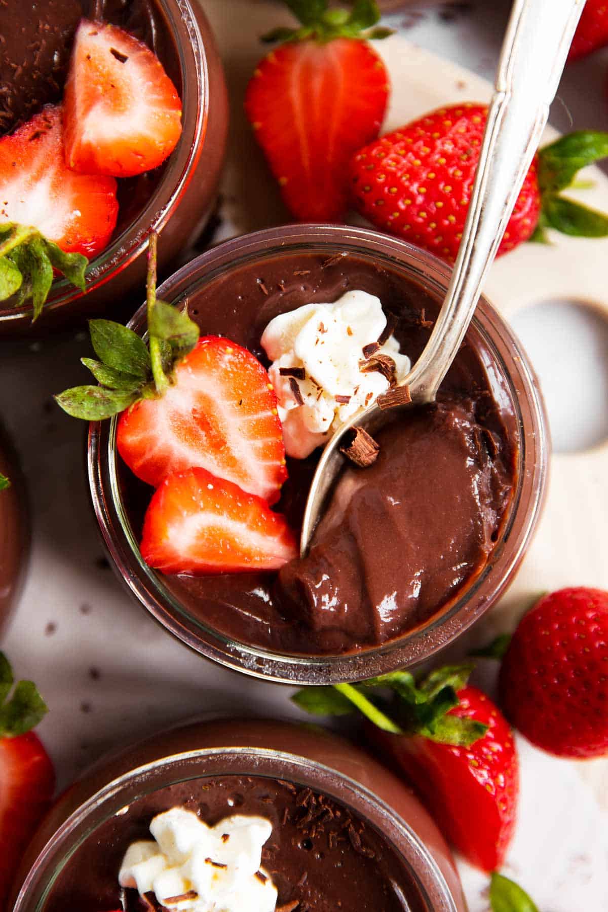 overhead view of chocolate pudding in glass cup with strawberries and whipped cream, with spoon stuck inside