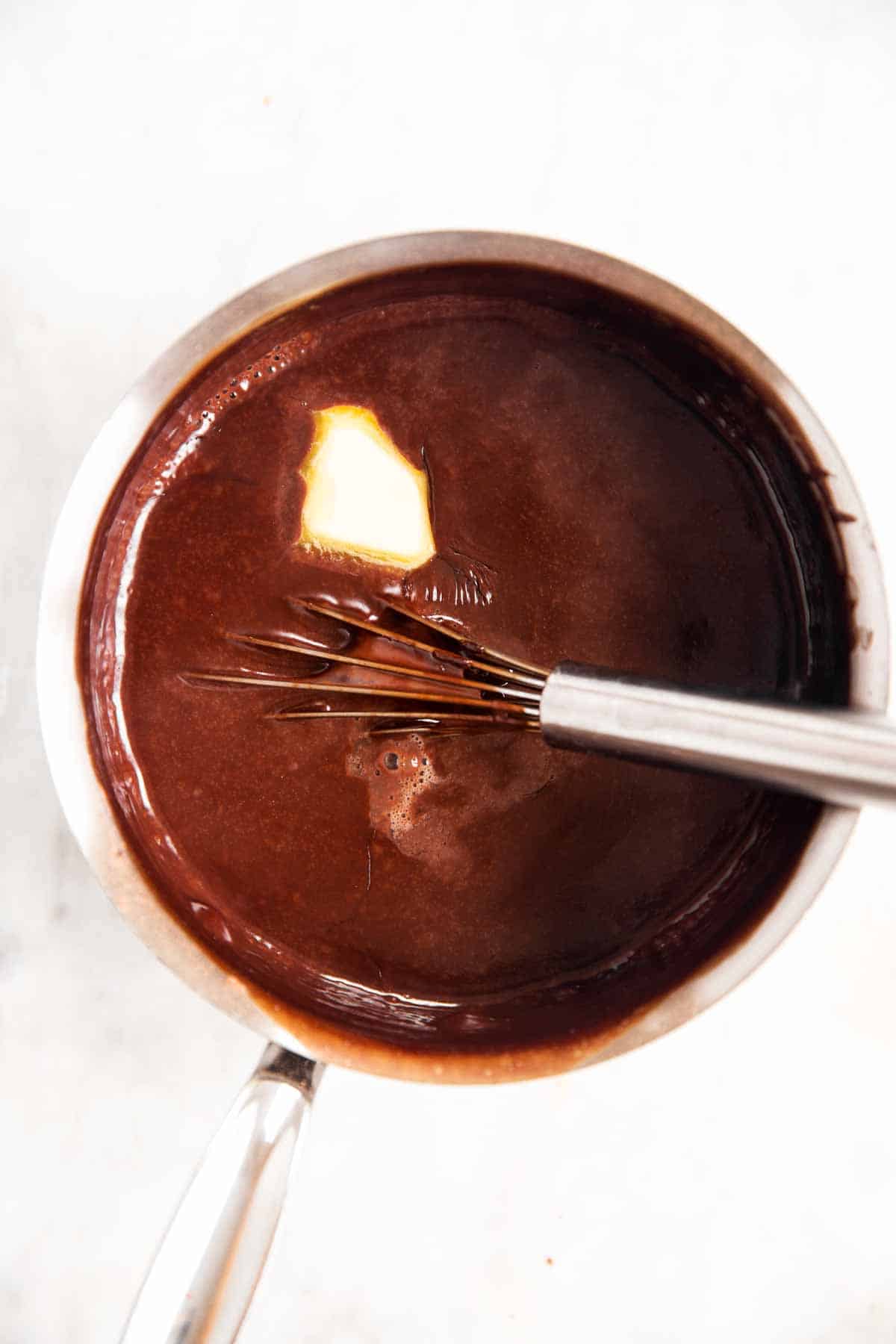 just-cooked chocolate pudding in saucepan with wire whisk, with melting pat of butter in pudding mixture