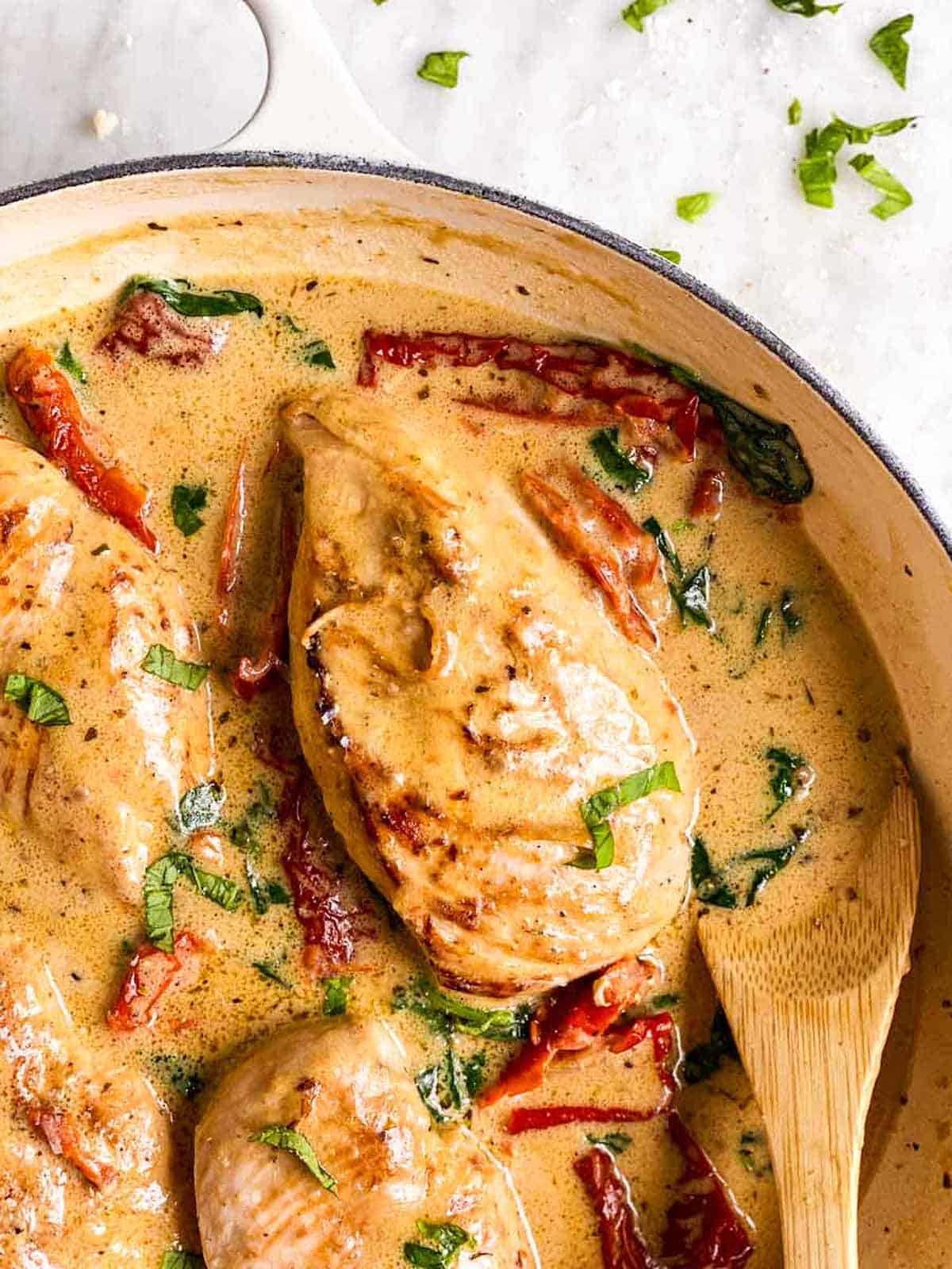 close up photo of chicken breast smothered in creamy tuscan sauce with sun-dried tomatoes and spinach