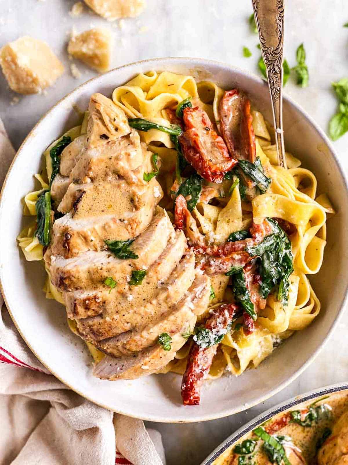 overhead view of sliced tuscan chicken breast in a white bowl with pasta and a fork stuck in