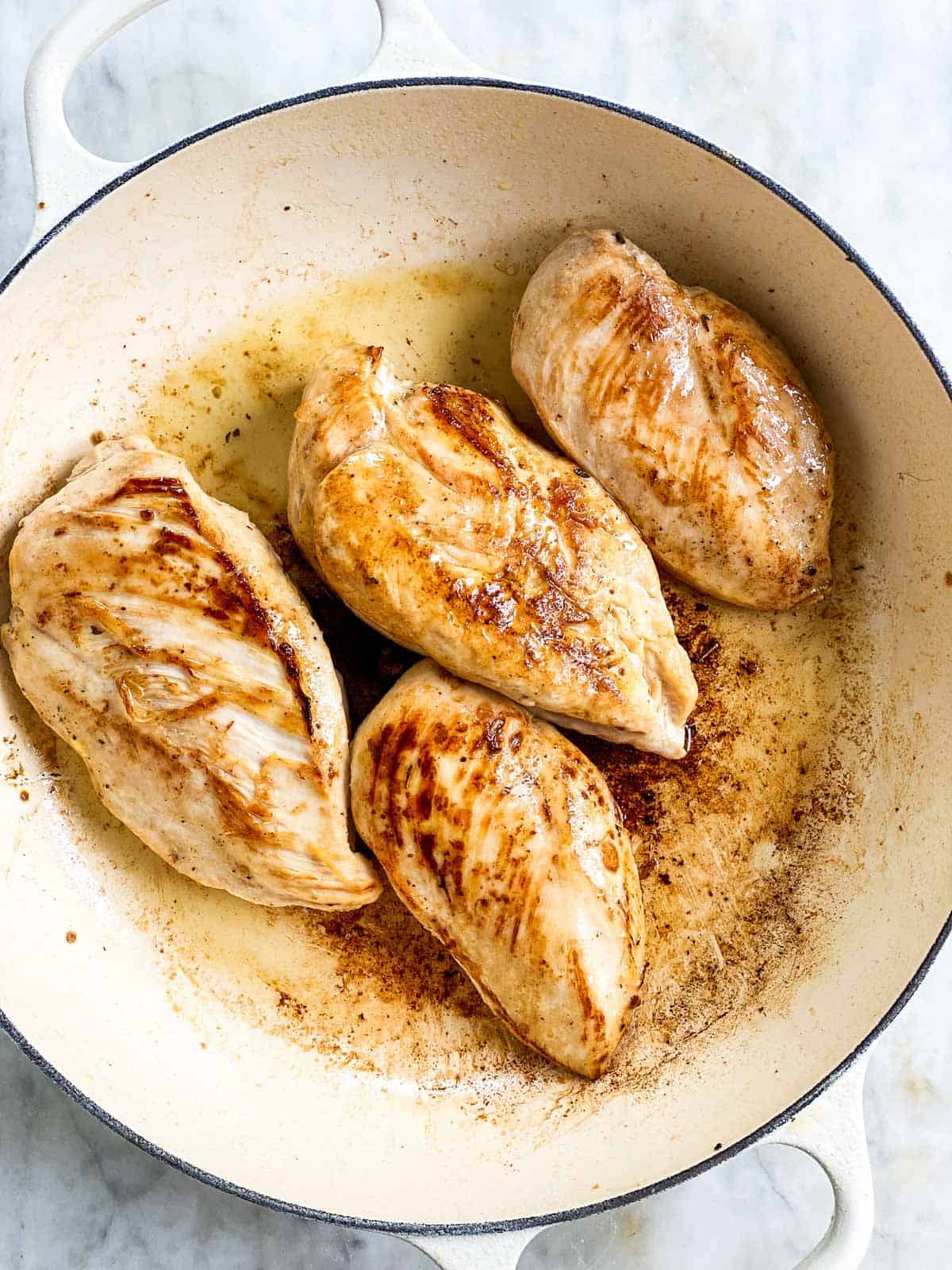 four browned chicken breast in white cast iron skillet